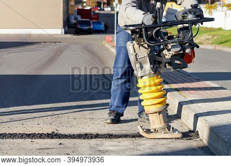 A Road Worker Uses A Portable Petrol Vibration Rammer To Repair Asphalt On The Driveway On A Bright 