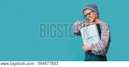 Caucasian Woman With Hat And Glasses Is Embracing A Present Smiling On A Blue Studio Wall With Free 