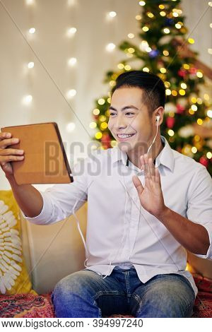 Positive Handsome Young Vietnamese Man Video Calling Friend On Christmas Eve