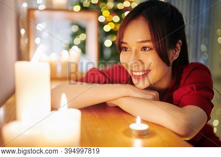 Happy Pretty Young Asian Woman Looking At Burning Candles And Making Wish On Christmas Eve