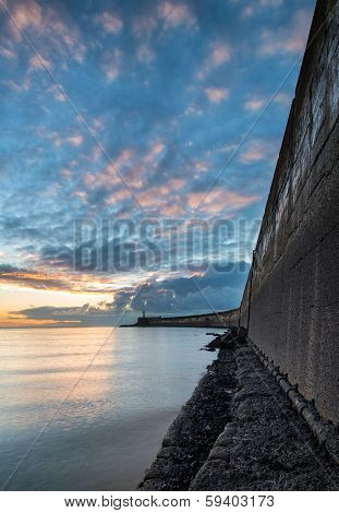 Beautiful Vibrant Sunrise Sky Over Calm Water Ocean With Lighthouse And Harbor Wall