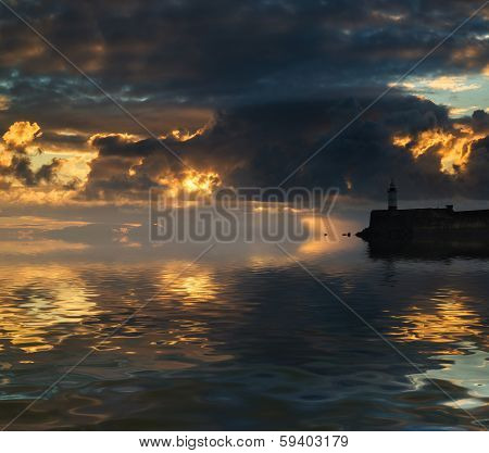 Beautiful Vibrant Sunrise Sky Over Calm Water Ocean With Lighthouse And Harbor Wall