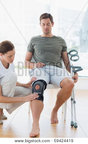 Female physiotherapist examining leg of man with crutches in hospital
