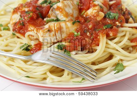 Fresh fish in arrabbiata sauce, served on spaghetti and with a fork, sprinkled with a parsely garnish, closeup