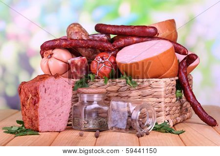 Lot of different sausages in basket on wooden table on natural background