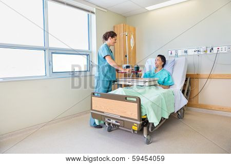 Happy nurse bringing breakfast for mature male patient in hospital room
