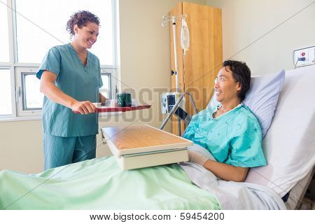 Happy friendly mid adult nurse bringing breakfast for mature patient in hospital