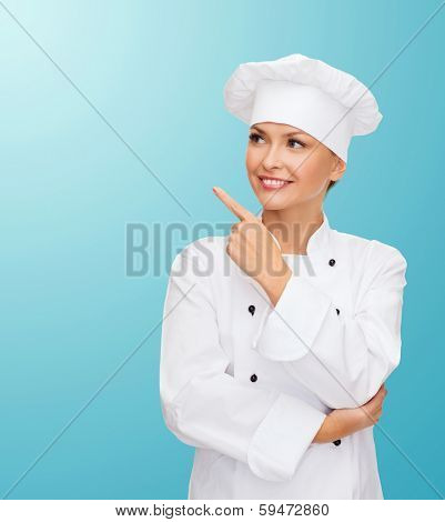 cooking, advertisement and food concept - smiling female chef, cook or baker pointing finger to something