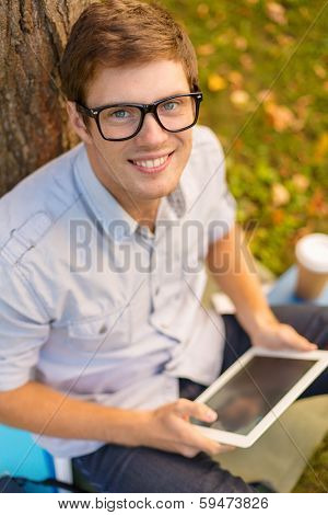 education, technology and internet concept - smiling male student in eyeglasses with tablet pc outside