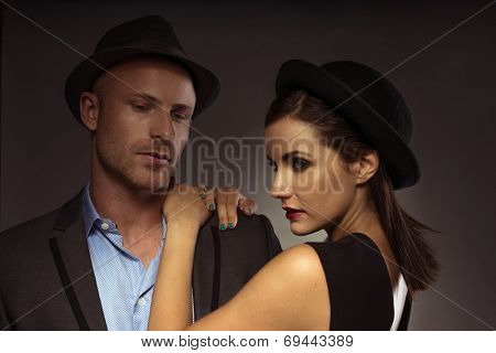Stylish elegant couple on a date standing in a close embrace in trendy eveningwear with the man looking down and the woman turning to smile seductively at the camera