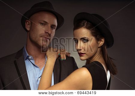 Stylish elegant couple on a date standing in a close embrace in trendy eveningwear with the man looking down and the woman turning to smile seductively at the camera