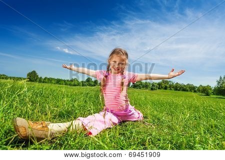 Girl makes leg-split on grass with arms apart