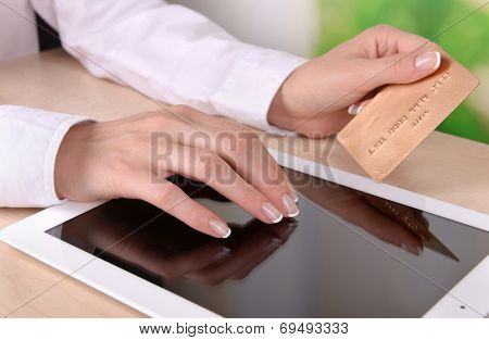 Female hands holding credit card and computer tablet on table on bright background