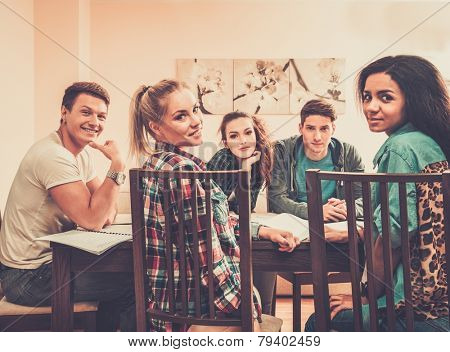 Multi ethnic group of students preparing for exams in home interior behind table 