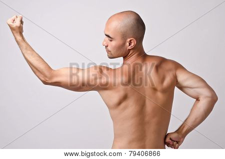 Fit bodybuilder from profile posing with his back.