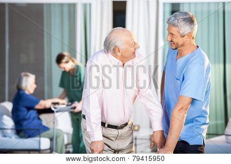 Happy male caretaker looking at disabled senior man at nursing home yard