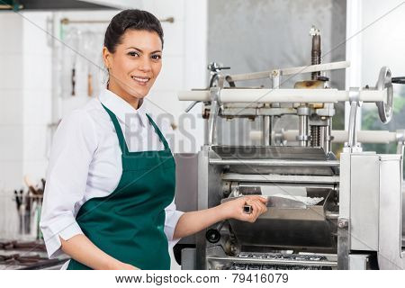 Portrait of happy female chef processing ravioli pasta in machine at commercial kitchen