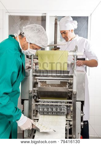 Chefs processing ravioli pasta in machine at commercial kitchen