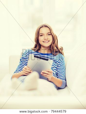 home, technology and internet concept - smiling teenge girl lying on the couch with tablet pc computer at home