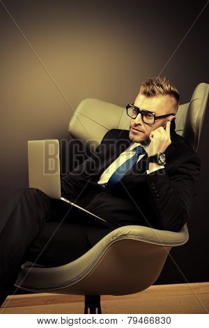 Imposing mature man in elegant suit sitting on a leather chair in a modern luxurious interior and working on a laptop. Fashion. Business.