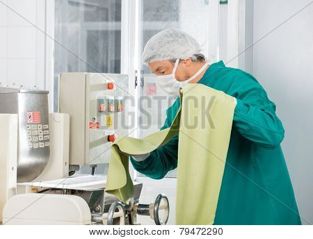 Male chef processing green spaghetti pasta sheet in machine at commercial kitchen