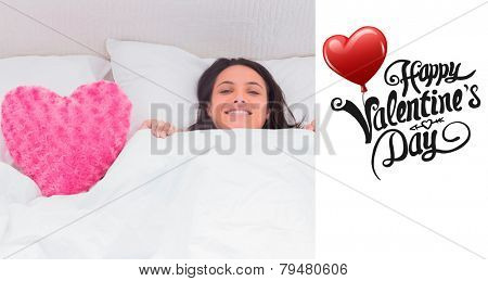 Woman lying in bed next to a fluffy heart pillow against cute valentines message
