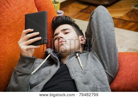Handsome young man at home reading with ebook reader