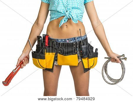 Plumber in shorts, shirt, tool belt with tools holding flexible hose and wrench