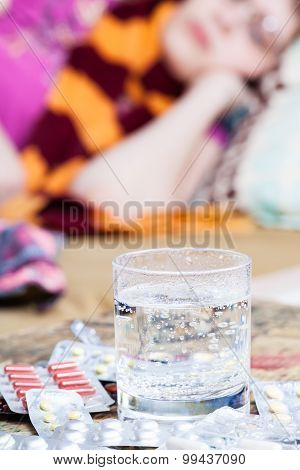 Glass With Medicament And Pile Of Pills On Table