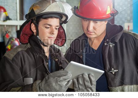 Young and mature firemen using tablet computer at fire station