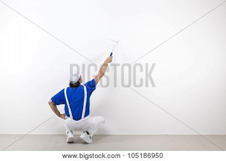 Squatting Painter With Paintroller On White Wall