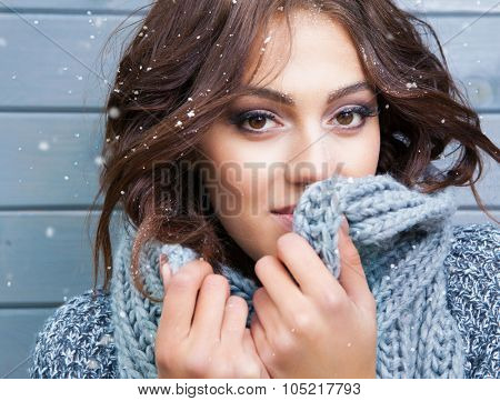 Beautiful natural looking young smiling brunette woman, wearing knitted scarf, covered with snow flakes. Snowing winter beauty concept
