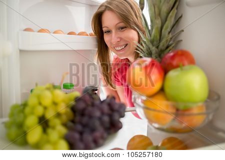 Smiling woman look at grape and apple in refrigerator