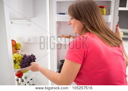 Young housewife take fresh sweet grapes from refrigerator