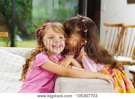 Brunette children sisters sitting happily on white livingroom sofa posing for camera with typical pi