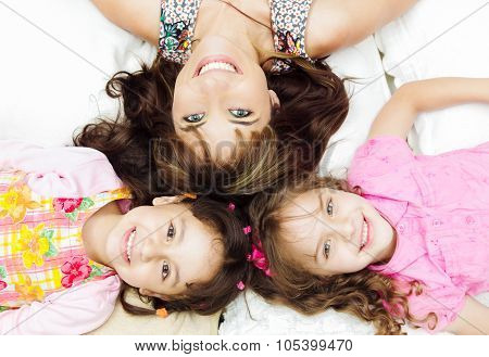 Young adorable hispanic sisters with mother lying down, heads touching and bodies spread out differe