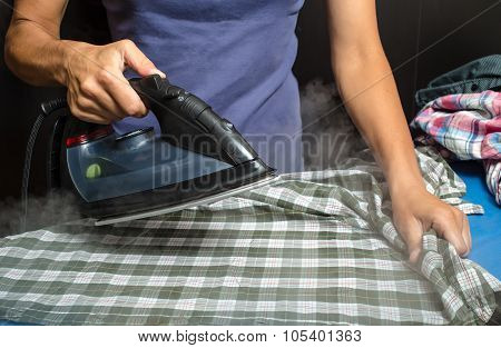 woman in a blue T-shirt ironing plaid shirt and other clothing