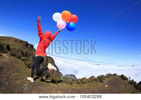 Cheering Young Woman Running On Mountain Peak With Colorful Balloons