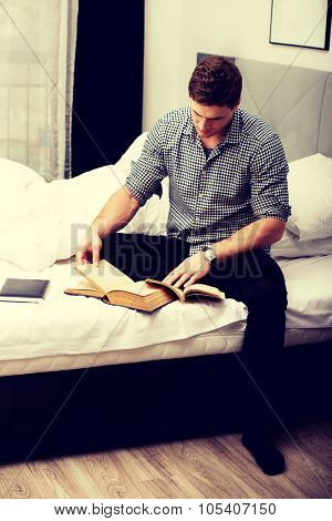 Handsome man reading a book in his bed.