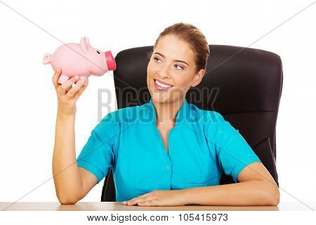 Young female doctor or nurse holding piggybank.