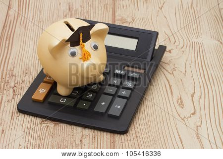 A Golden Piggy Bank With Grad Cap And Calculator On Wood Background