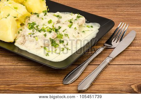 Slices of pork tenderloin with potatoes stewed in cream saucem, served on the black plate.