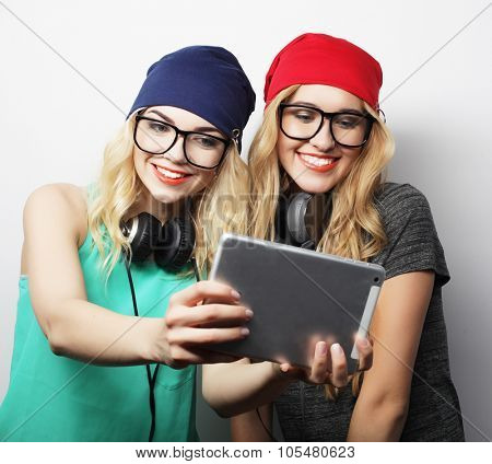 two hipster girls friends taking selfie with digital tablet, studio shot over gray vackground
