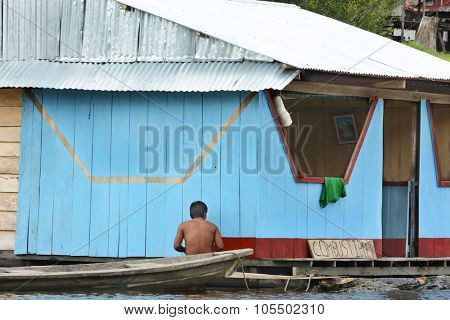 IQUITOS, PERU - OCTOBER 13, 2015: Man painting fuel dock. Along an Amazon River tributary an indigenous man paints a  res stripe on fuel dock building.