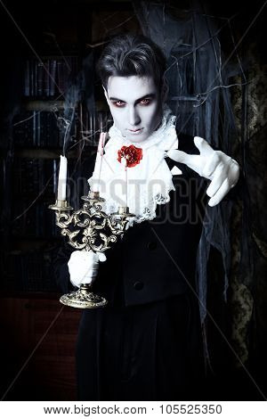 Handsome vampire man wearing elegant tailcoat stands in the old medieval castle. Halloween.