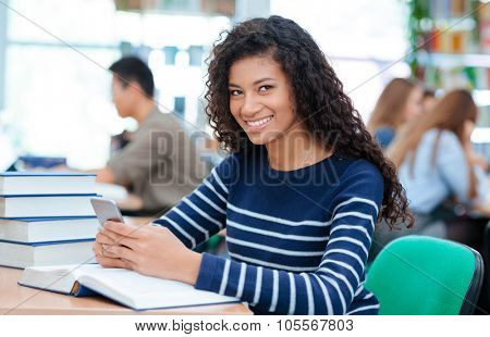 Portrait of a afro american woman sitting at the table with smartphone in university classrom and looking at camera