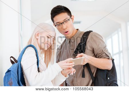 Portrait of a happy students using smartphone in the university hall
