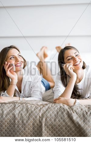 Two Beautiful Girls Talking And Smiling While Lying On A Bed