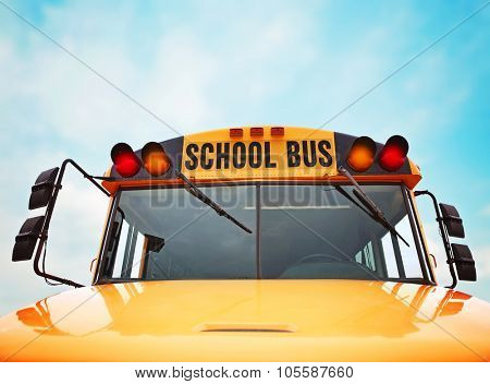 wide angle front view of a bright yellow orange school bus on a sunny summer day with clouds in the sky toned with a retro vintage instagram filter app or action effect
