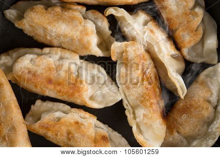 Close up cooking fried dumplings in a frying pan. Chinese dish with hot steams, on rustic vintage wooden background. 